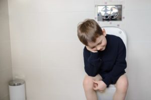 Menino sentado no vaso do banheiro cabisbaixo por estar com constipação intestinal infantil.