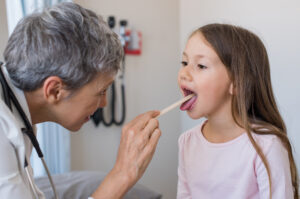 Um médica examinando a garganta de uma menina que tem dor de garganta com um abaixador de língua.