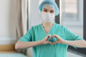 Enfermeira fazendo um coração com as mãos. Representação do papel do enfermeiro e da equipe de enfermagem.