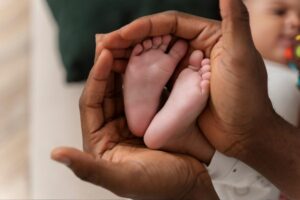 Mãos de enfermeira segurando os pés de um recém nascido. Representação do teste do pezinho.