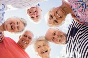 Grupo de idosos sorridentes visto de baixo pra cima. Representação de cuidados essenciais com a saúde do idoso.