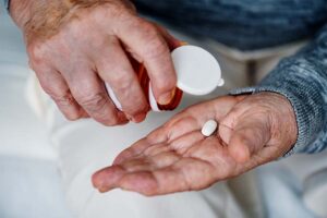 Close de idoso despejando um comprimido de um frasco na mão. Representação de gerenciamento de medicamentos na terceira idade.