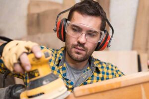 Homem trabalhando com madeira. Ele está usando óculos de proteção para evitar que não ocorra nenhuma lesão ocular. Representação de lesões oculares: prevenção e primeiros socorros.
