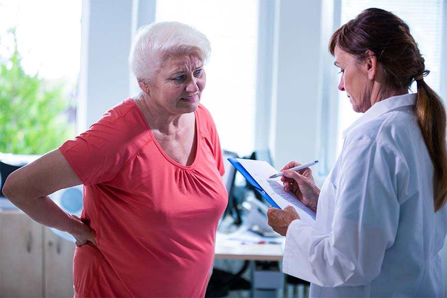 Paciente idosa com dor crônica sendo atendida por uma médica. Representação de como melhorar a dor crônica.