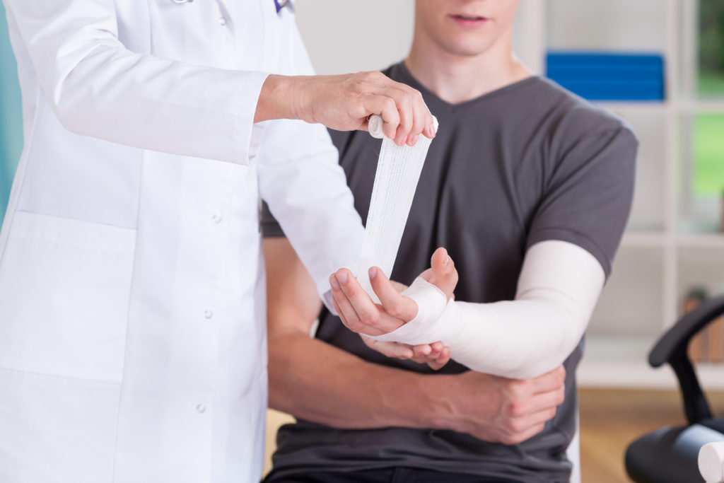 Médico enfaixando braço de um homem devido a fratura do escafóide