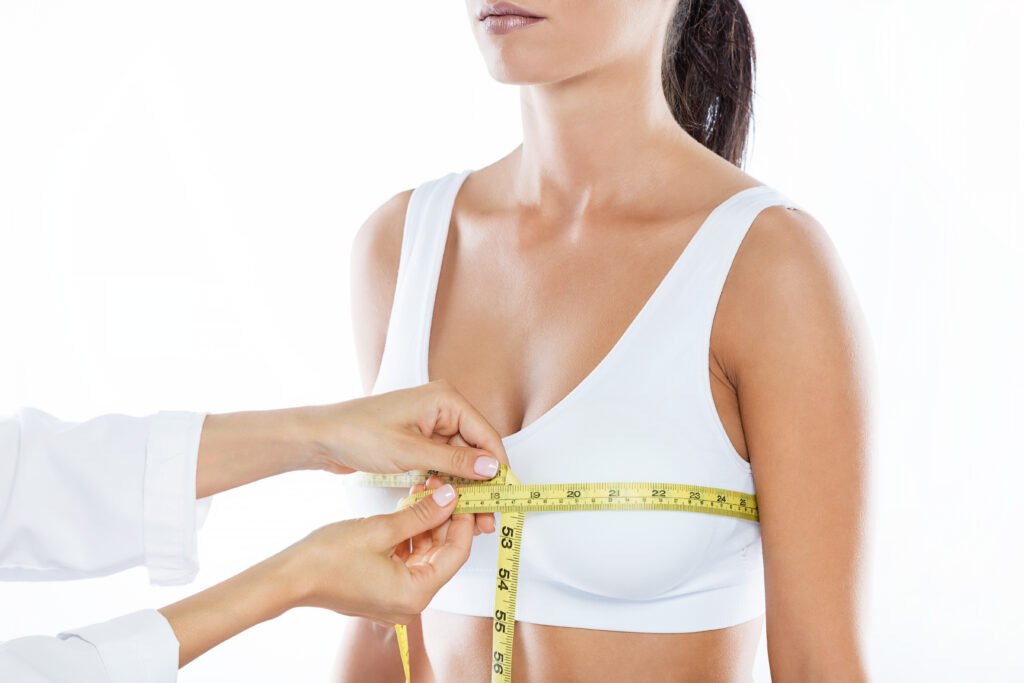 Médico com um fita métrica medindo um dos seios de uma mulher que pretende fazer uma mamoplastia redutora